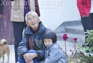留守兒童偎依在爺爺的懷里怯怯地眼神卻透露出想參與游戲的渴望